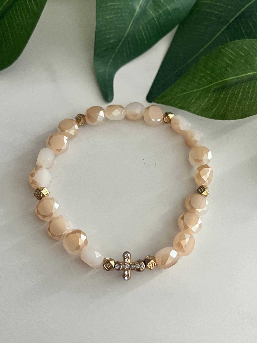 Beige faceted bead cross bracelet with gold cross charm on a stretchy band.