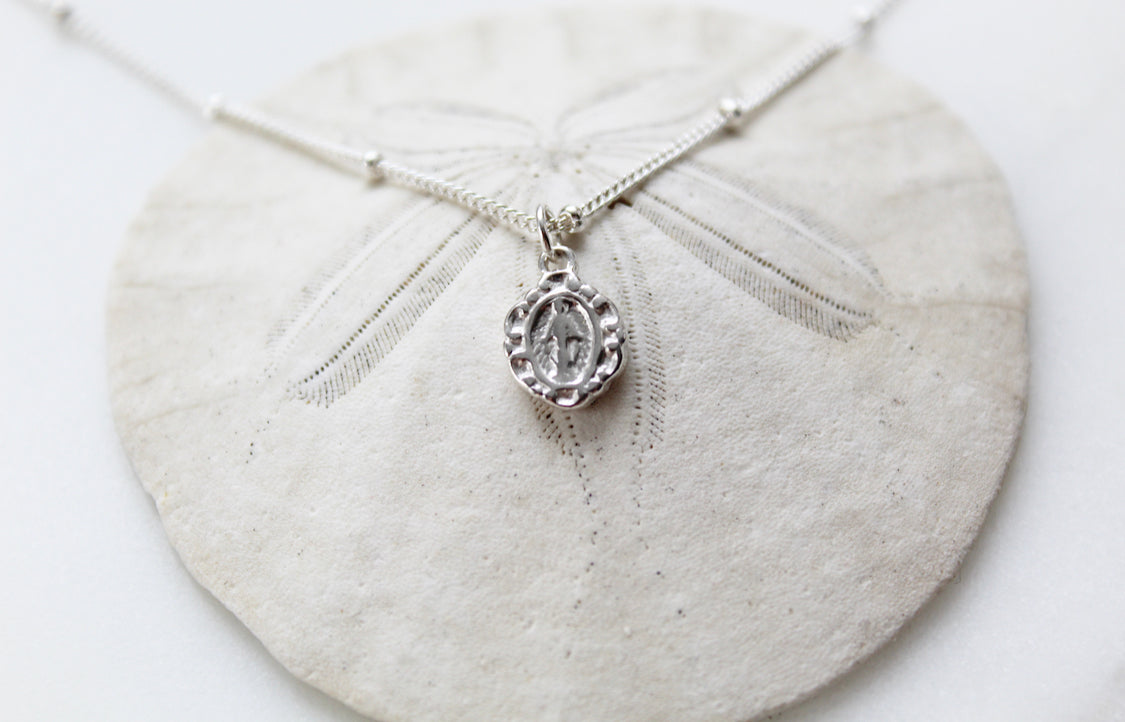 Sterling silver tiny medal necklace with oval pendant and fine chain, laid on cloth