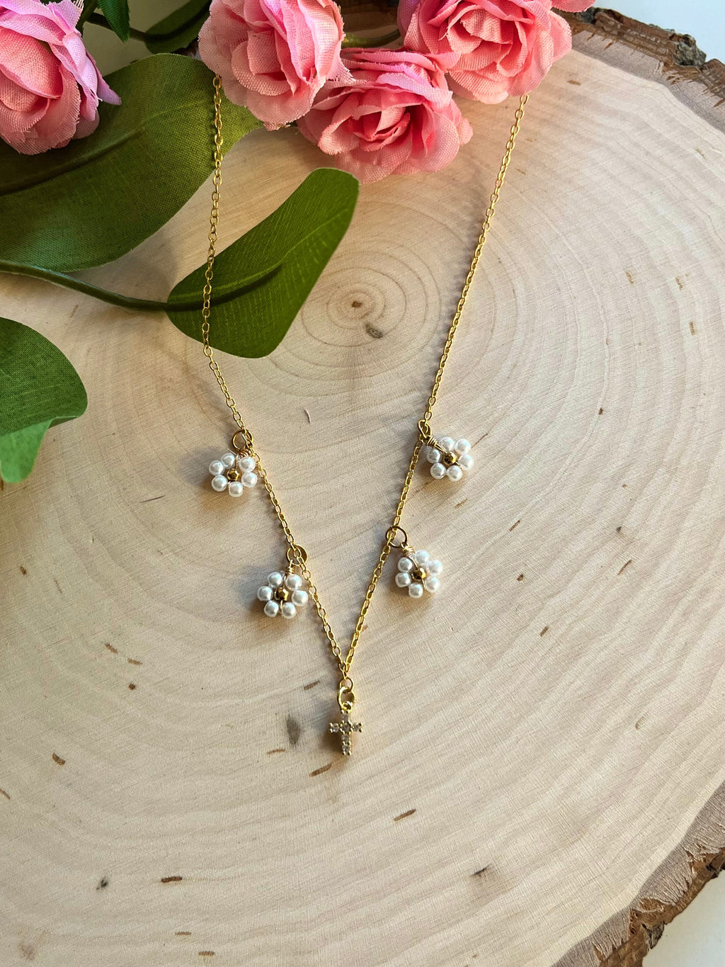 Gold necklace with cross pendant and small white daisy charms on a chain
