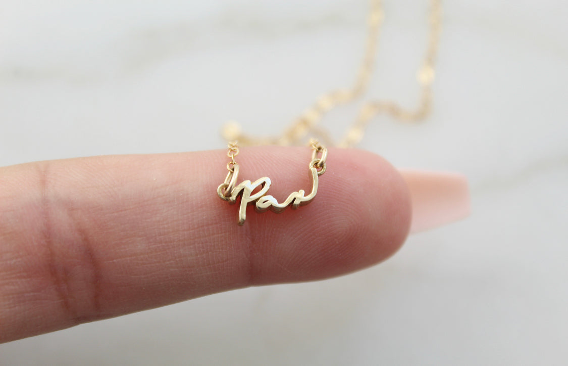Gold Pax pendant necklace close-up in hand with thin link chain