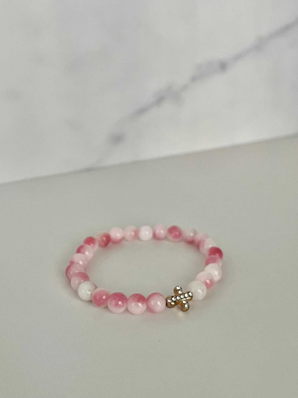 Pink beaded bracelet with gold cross charm, featuring alternating light pink beads.