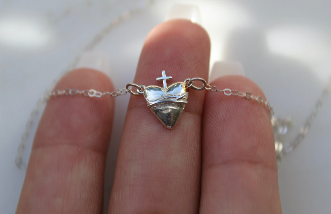 Sterling silver heart pendant with cross and chain, close-up on fingers