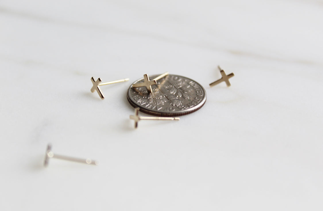 Gold-tone cross stud earrings with round coin for size comparison on a flat surface.