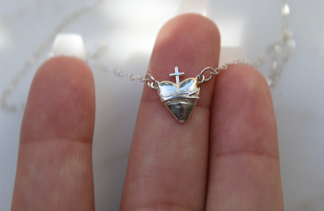 Sterling silver heart pendant and small cross on chain, held in fingers