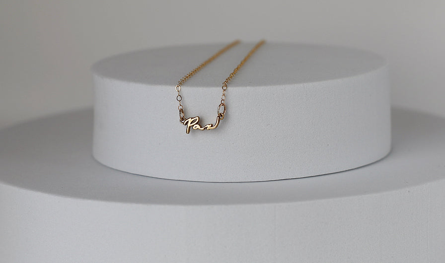 Gold Pax pendant necklace on white display pedestal with fine link chain
