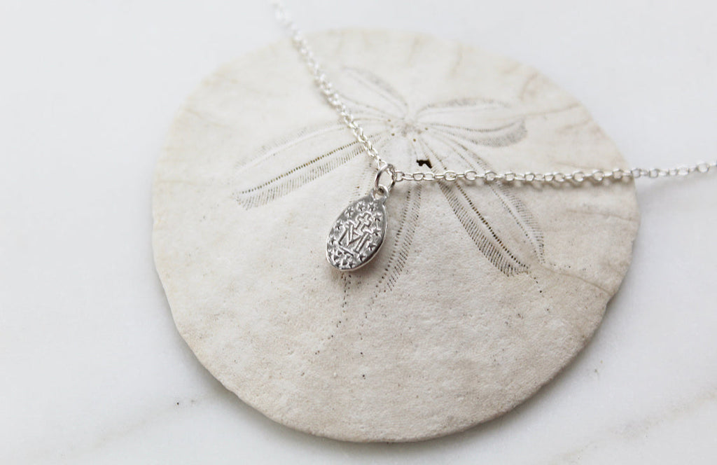 Oval sterling silver medal pendant on chain with decorative rays, close-up