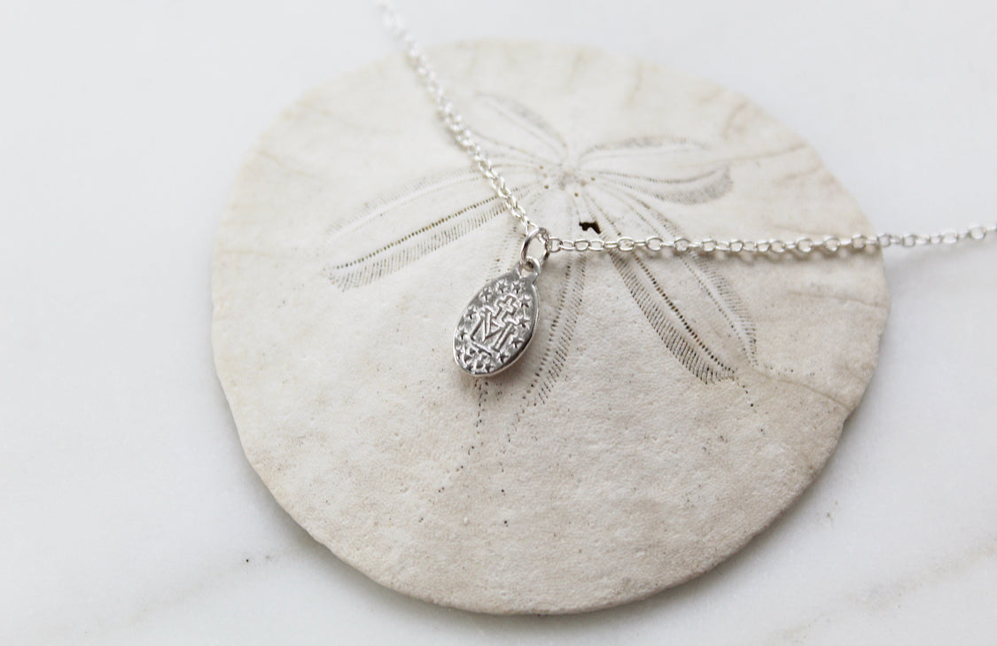 Oval sterling silver medal pendant on chain with decorative rays, close-up