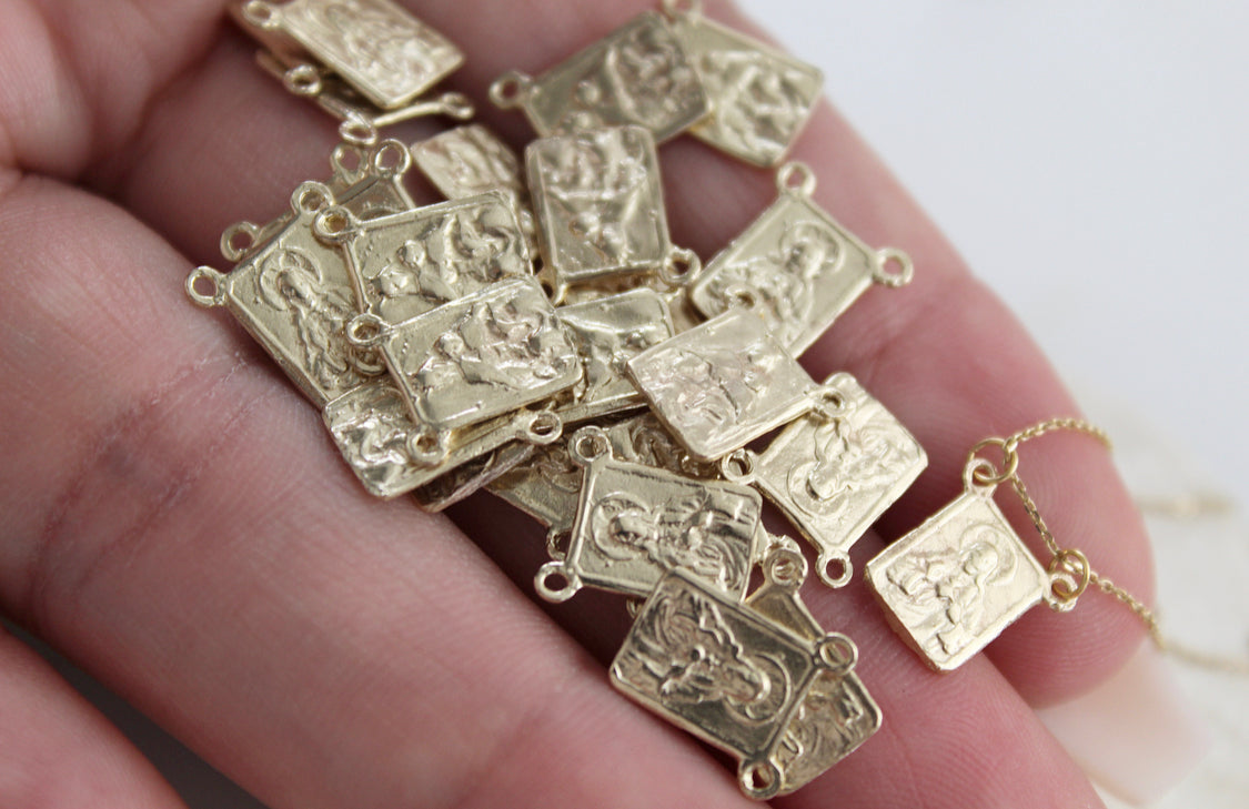 Scapular necklace charms spread on palm with gold chain