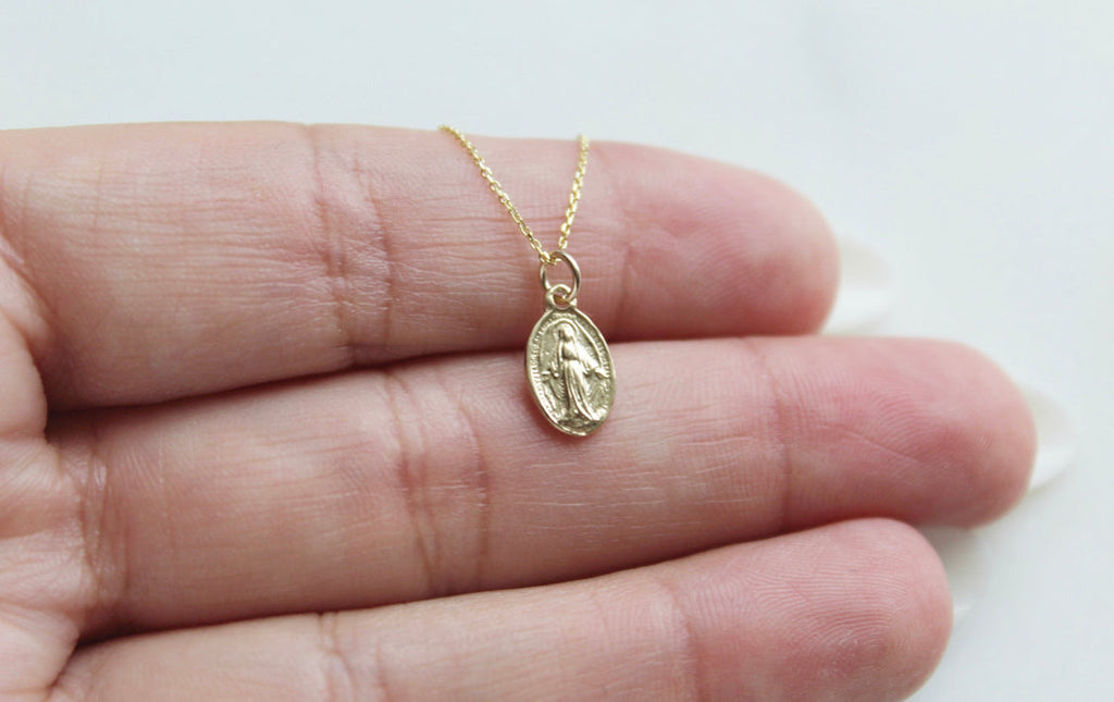 14k gold miraculous medal necklace pendant held in an open palm on chain