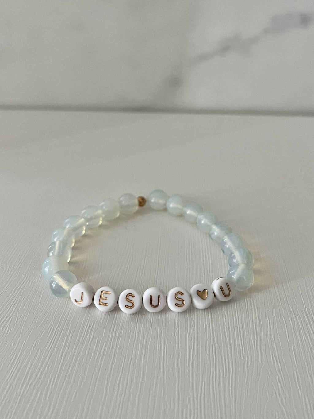 Clear bead bracelet with white letter beads spelling "JESUS U"