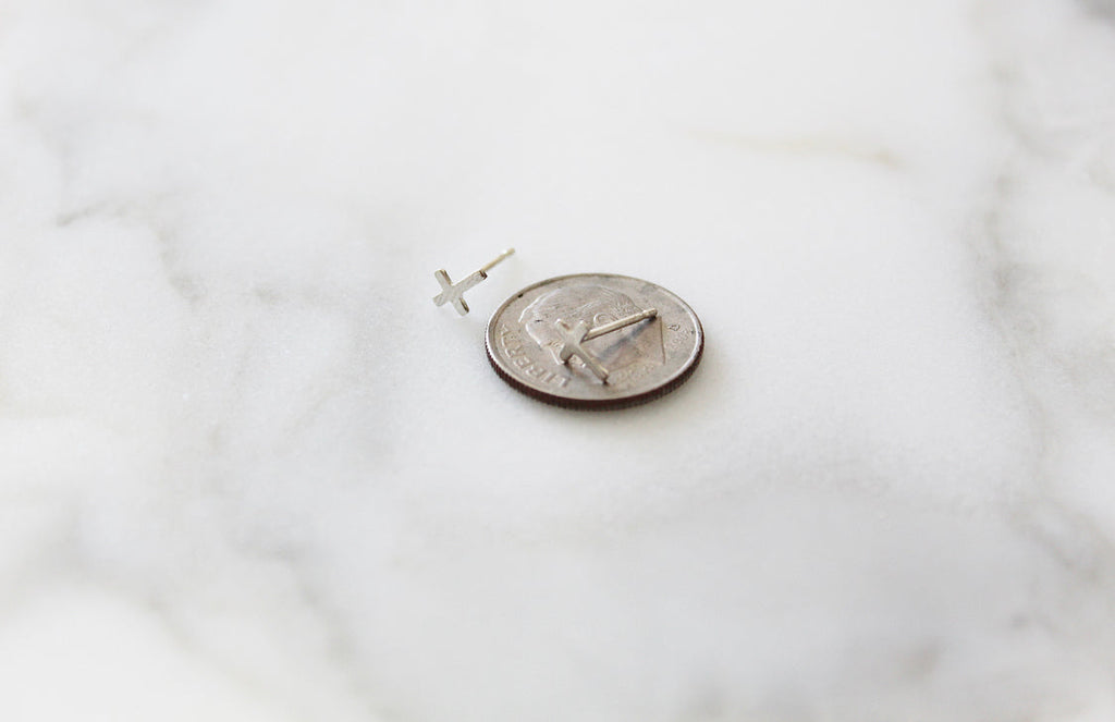 Sterling silver cross stud earring beside a coin for size reference.