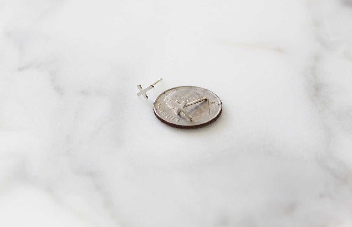 Sterling silver cross stud earring beside a coin for size reference.