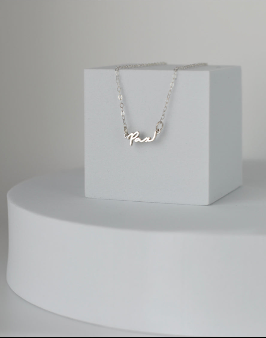 Sterling silver Pax necklace with cursive Pax pendant hanging from a fine chain