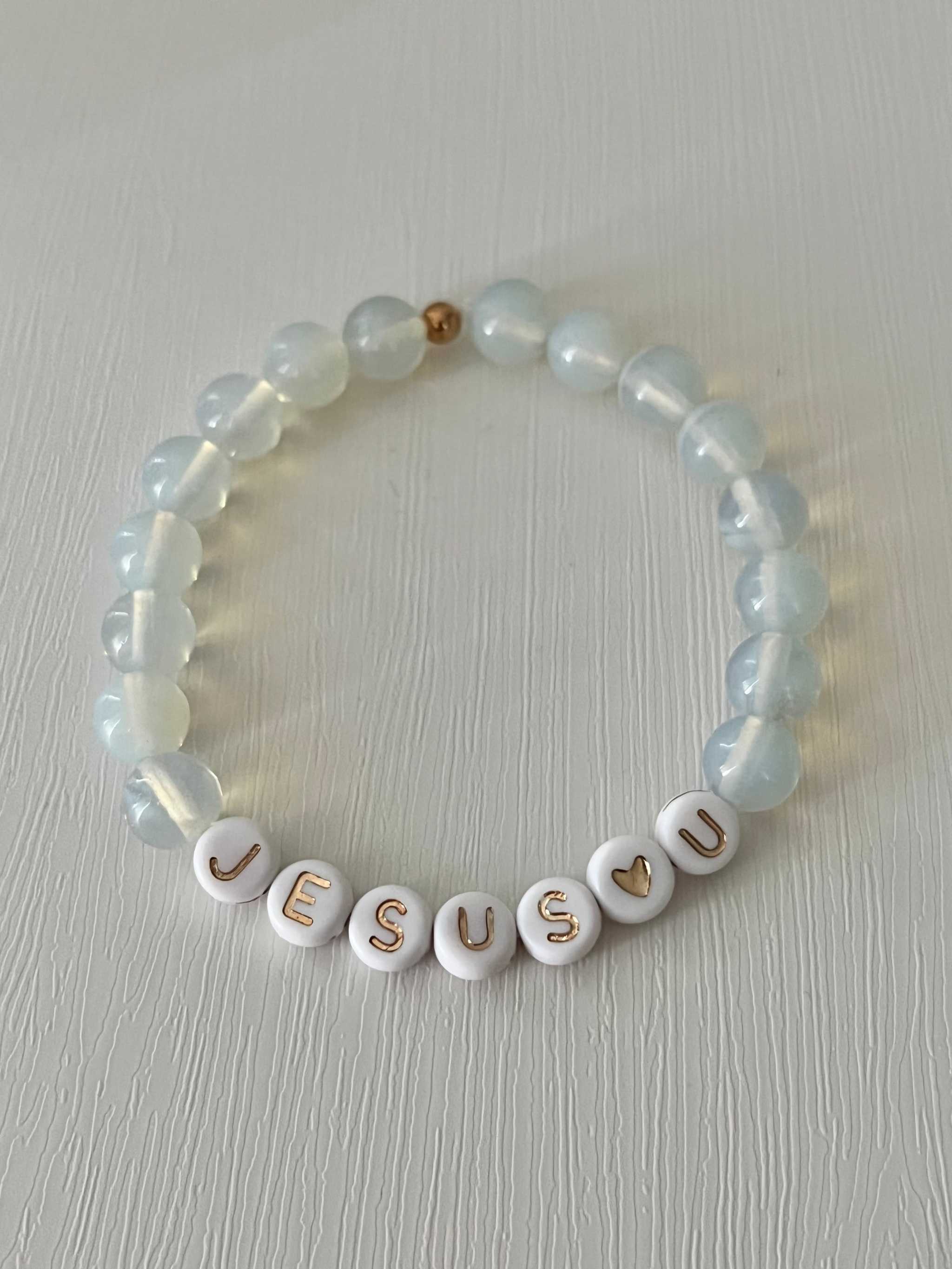 Clear bead bracelet with white letter beads spelling "JESUS U" and a heart charm