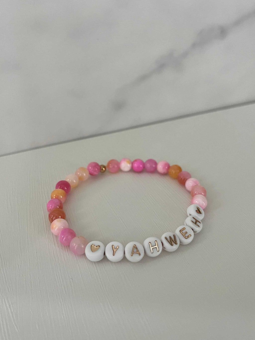 Pink beaded stretch bracelet with white letter charms spelling YAHWEH and heart accents.