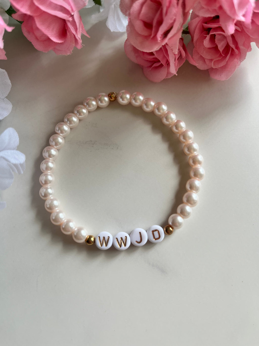 Pearl bead bracelet with small gold-letter beads spelling WWJD and white round pearls.