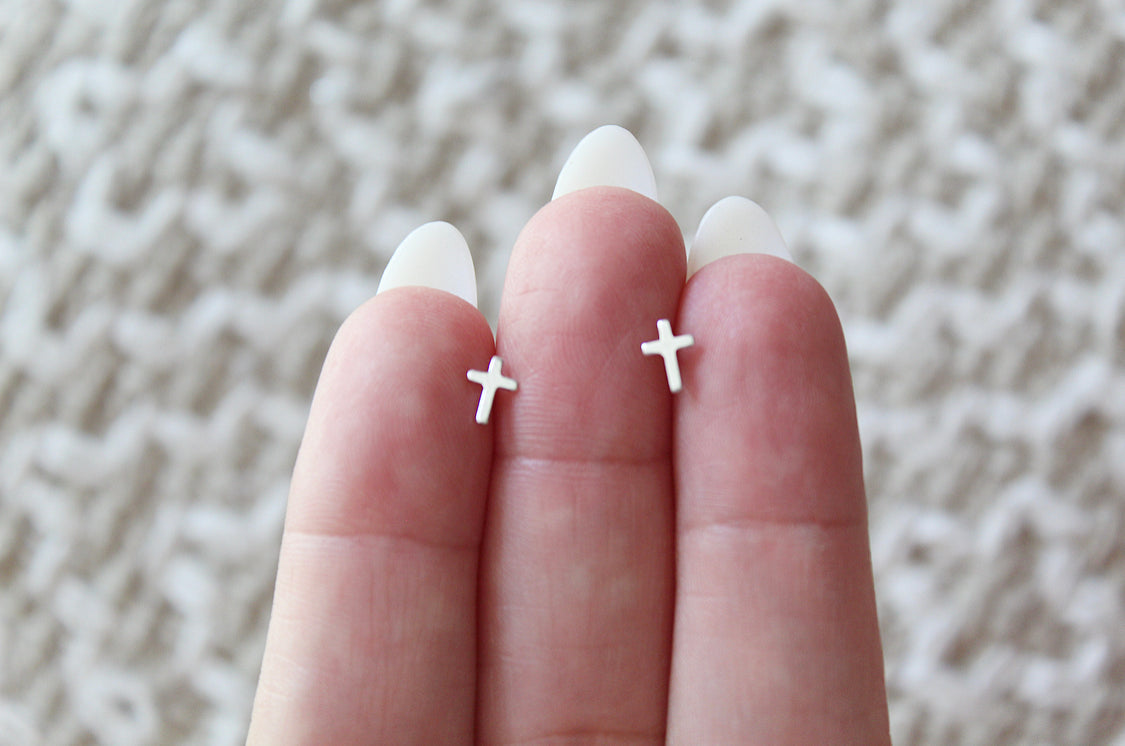 Sterling silver cross stud earrings on fingertips, pair of cross charms shown.