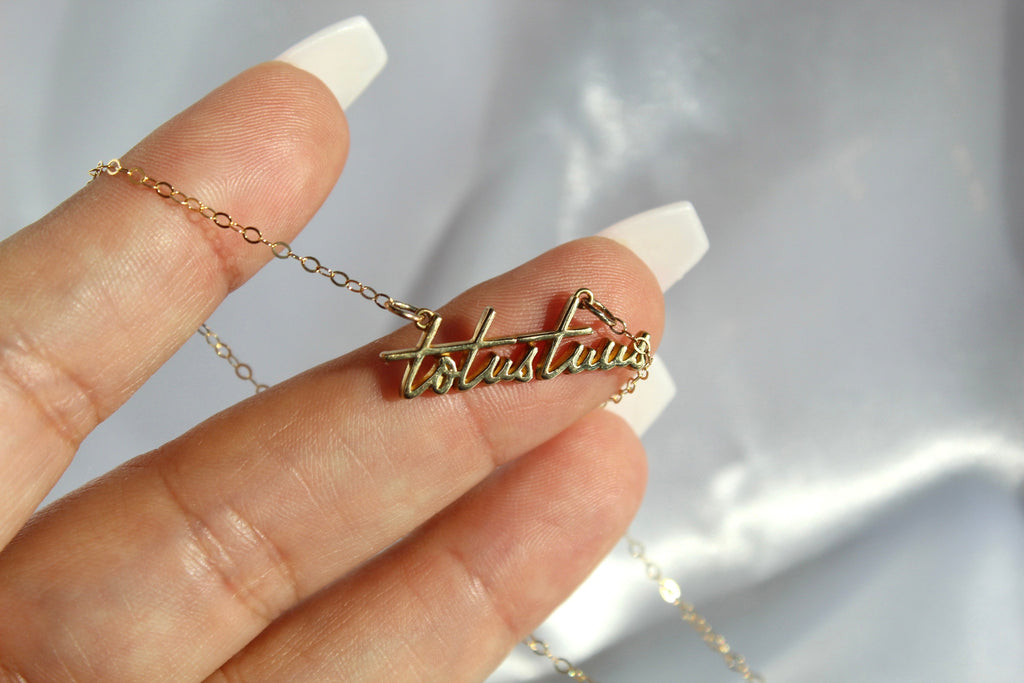 Gold-tone script pendant necklace with cross charm held in hand