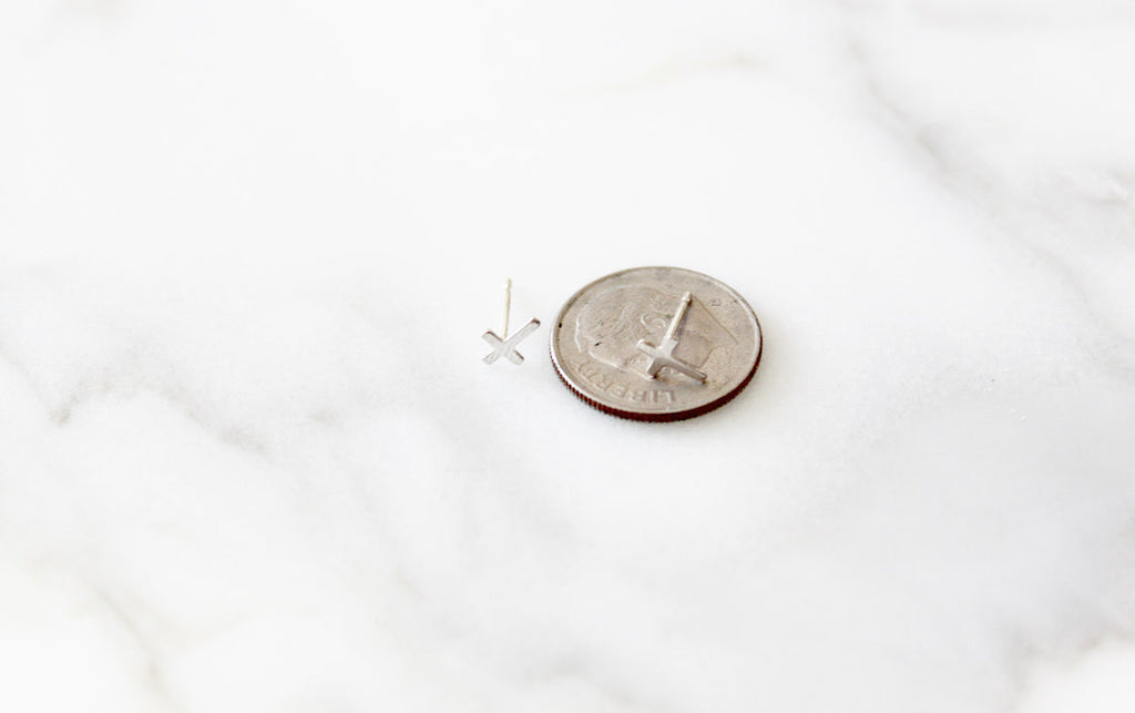 Sterling silver cross stud earring beside a coin for size reference.