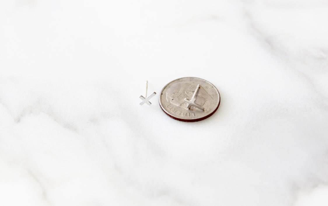 Sterling silver cross stud earring beside a coin for size reference.