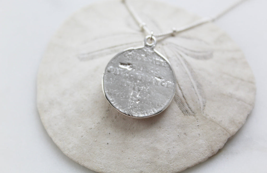 Silver round sacred heart coin pendant with a small bail on a chain.