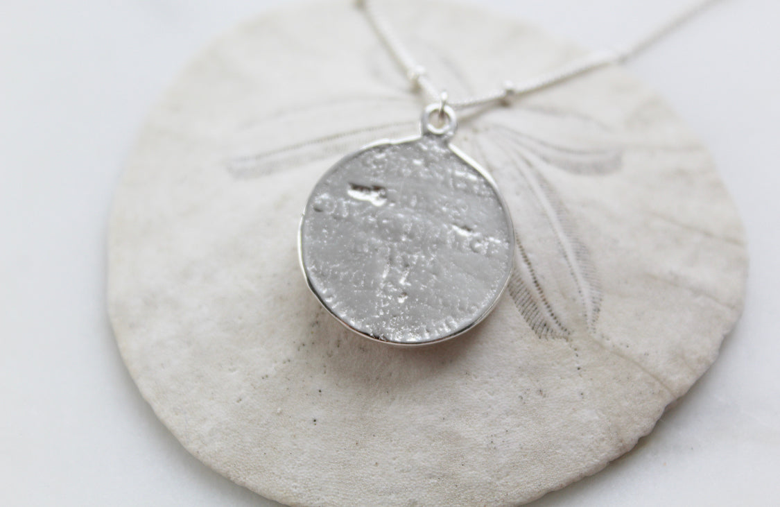 Silver round sacred heart coin pendant with a small bail on a chain.