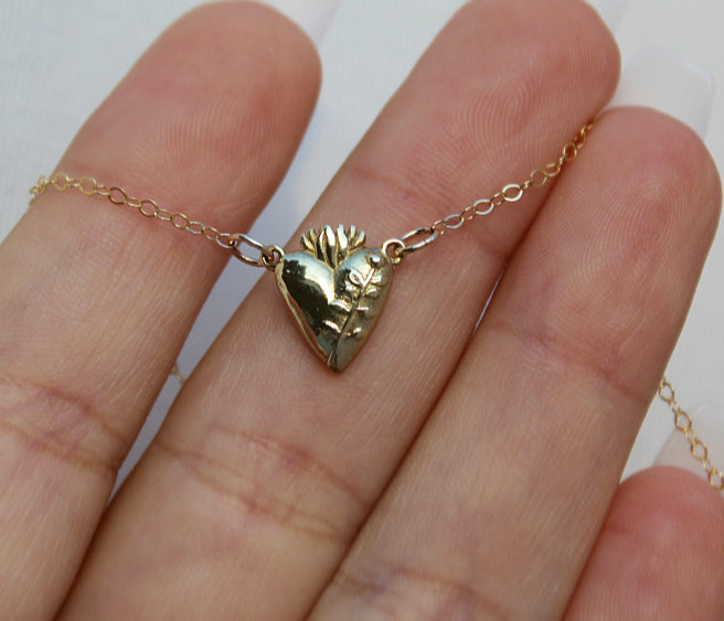 Gold heart pendant necklace shown on open palm, chain with floral detail
