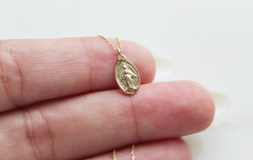 14k gold miraculous medal necklace pendant on chain held between fingers