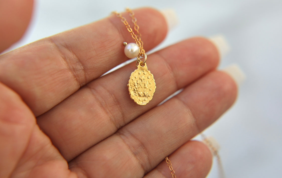 Gold-tone medal necklace with pearl bead and oval textured pendant on chain
