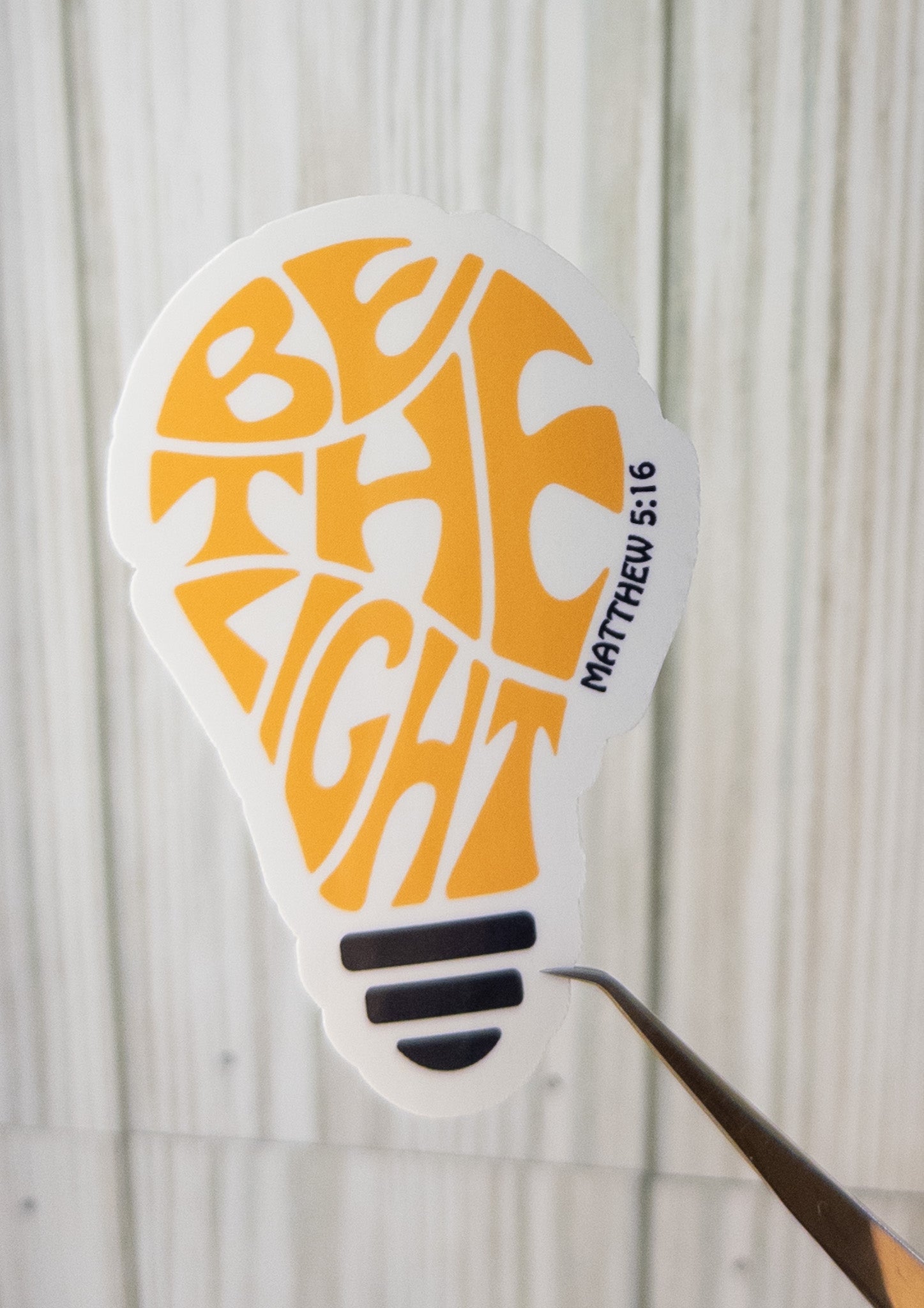 Bulb-shaped sticker with orange letter art and 'Matthew 5:16' text