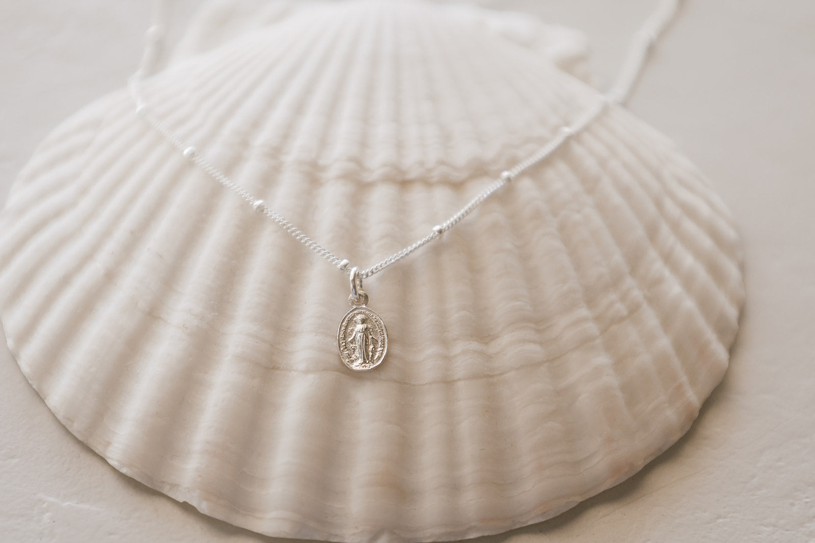 Silver-tone miraculous medal necklace with oval pendant on delicate chain, flat lay