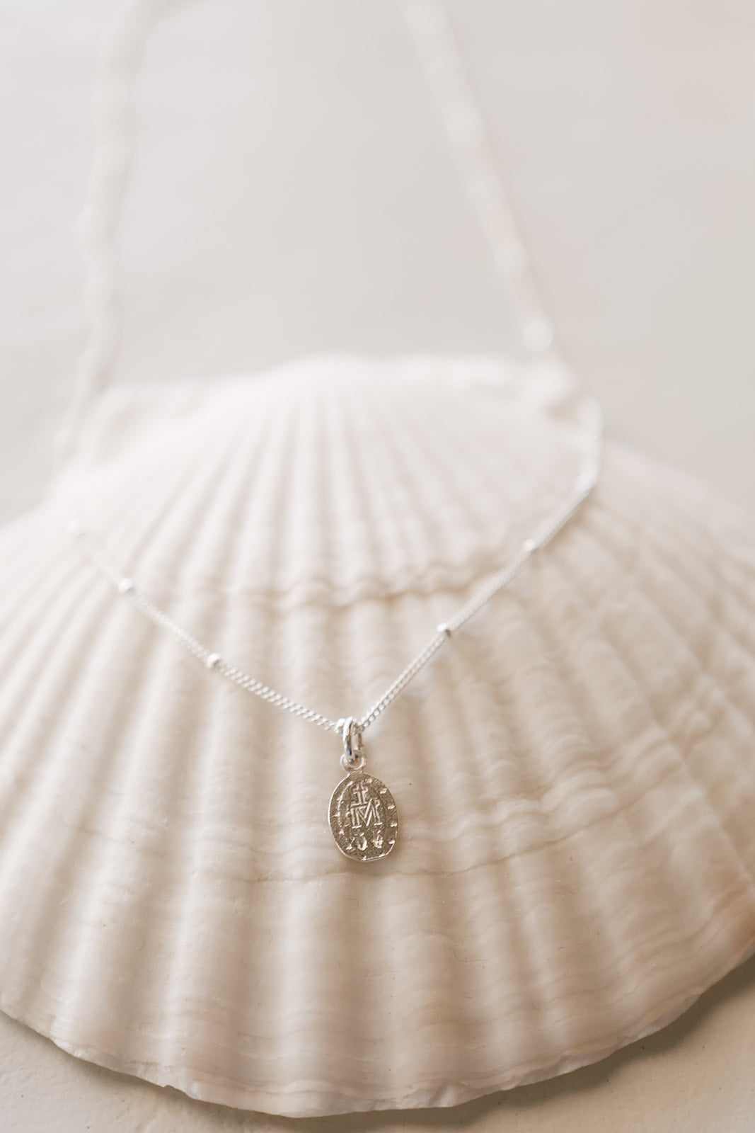Silver-tone chain necklace with oval miraculous medal pendant on seashell surface