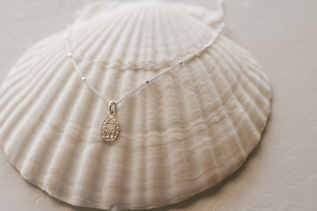Sterling silver fine-chain necklace with oval medal charm, on seashell