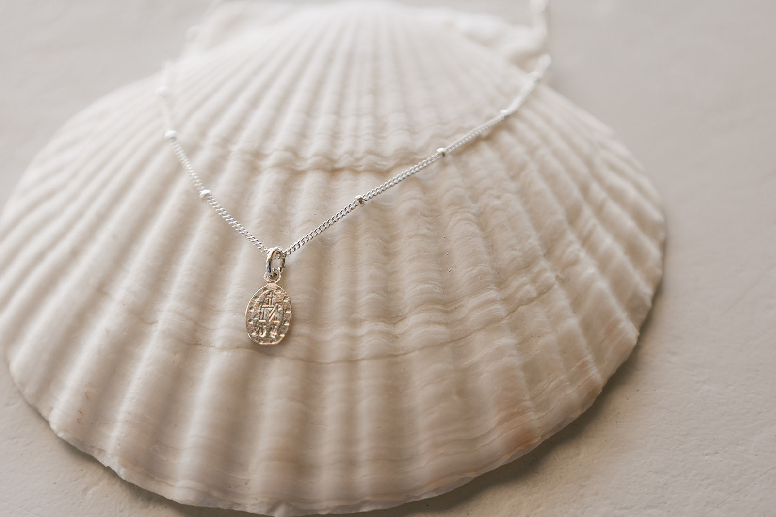 Sterling silver fine-chain necklace with oval medal charm, on seashell