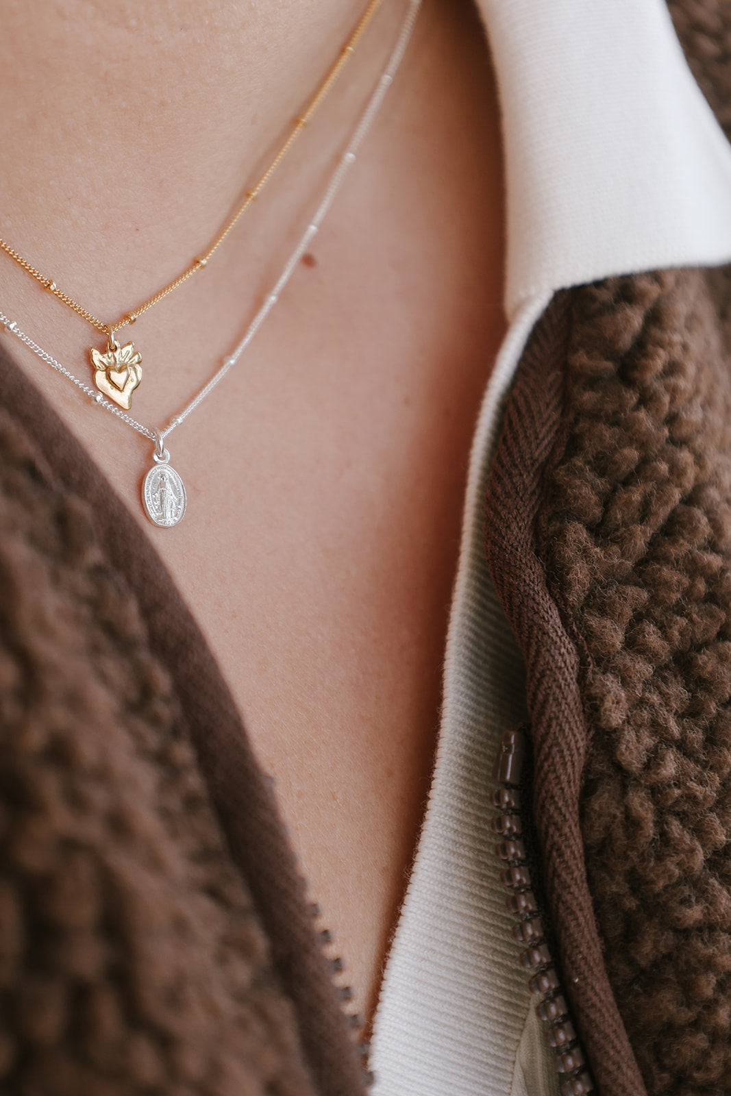 Layered heart charm necklace with gold heart pendant and silver oval pendant on chains