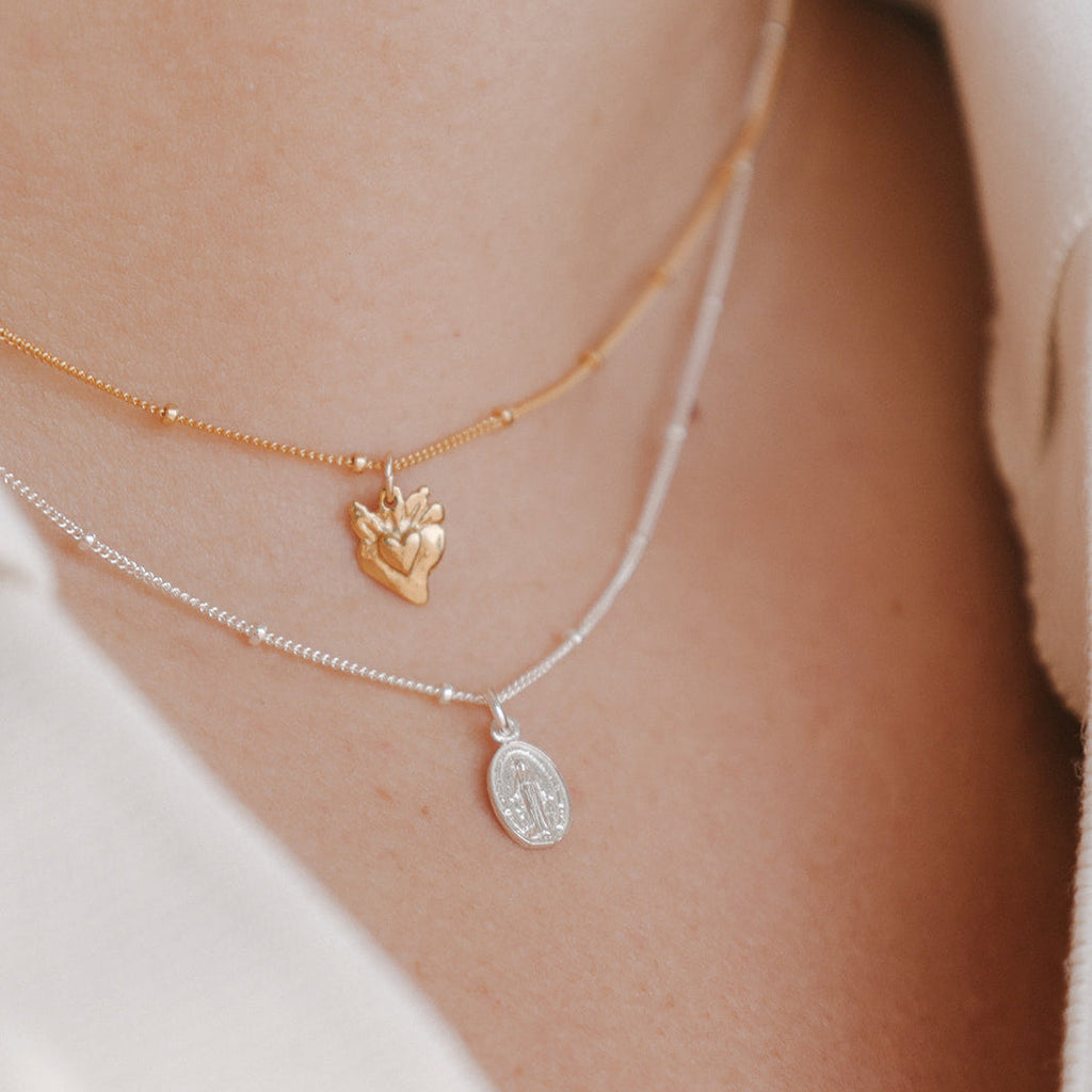 Layered heart charm necklace with gold heart pendant and silver oval pendant on chains