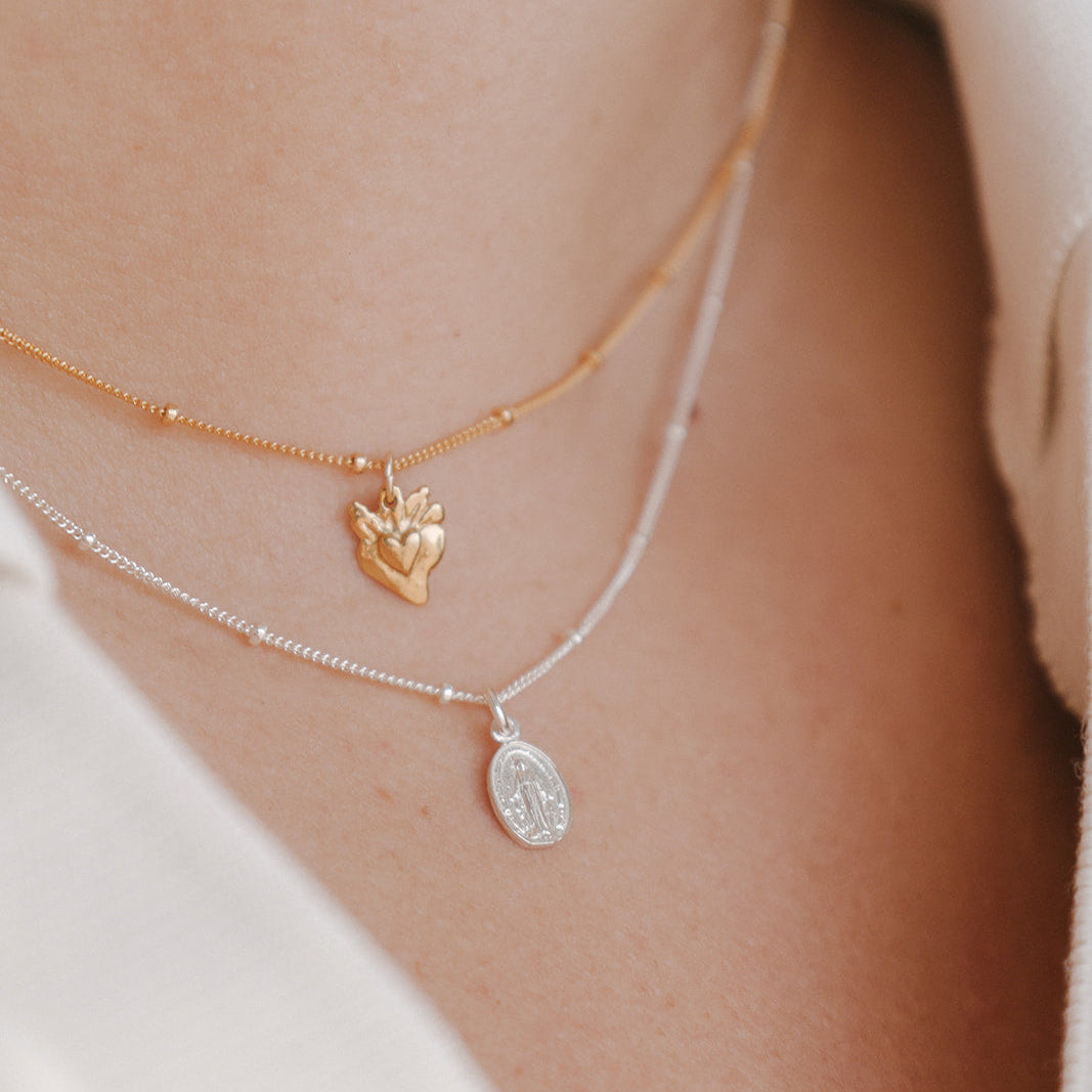 Layered heart charm necklace with gold heart pendant and silver oval pendant on chains