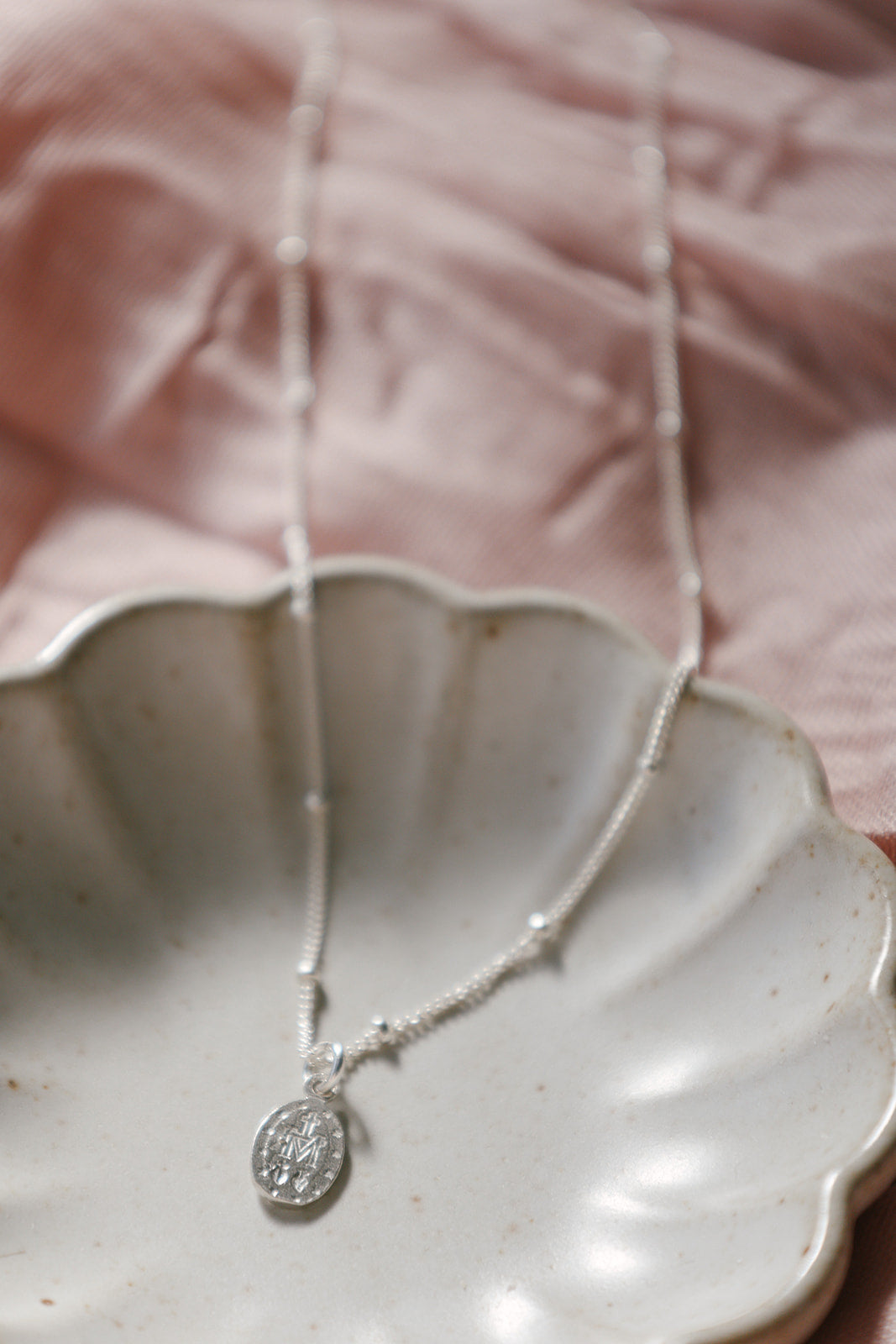 Sterling silver oval medal pendant necklace over heart-shaped dish