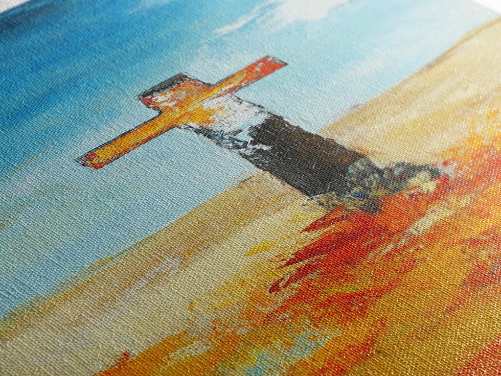 Textured cross painting close-up with blue sky, tan ground, and orange brushstrokes