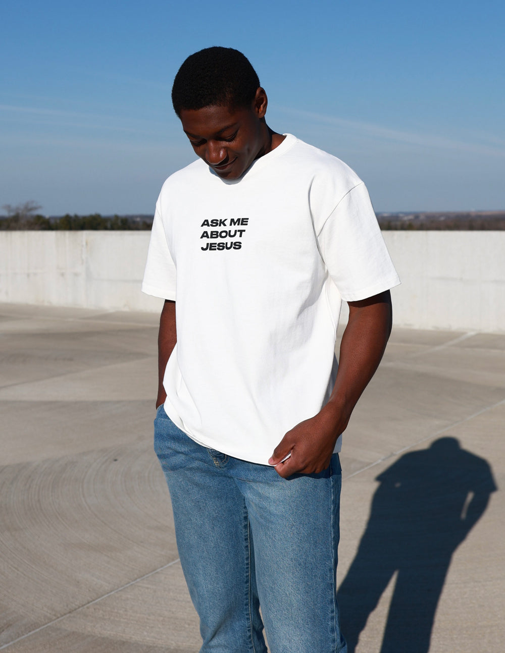 White heavyweight T-shirt with black chest text: Ask Me About Jesus, standing pose.