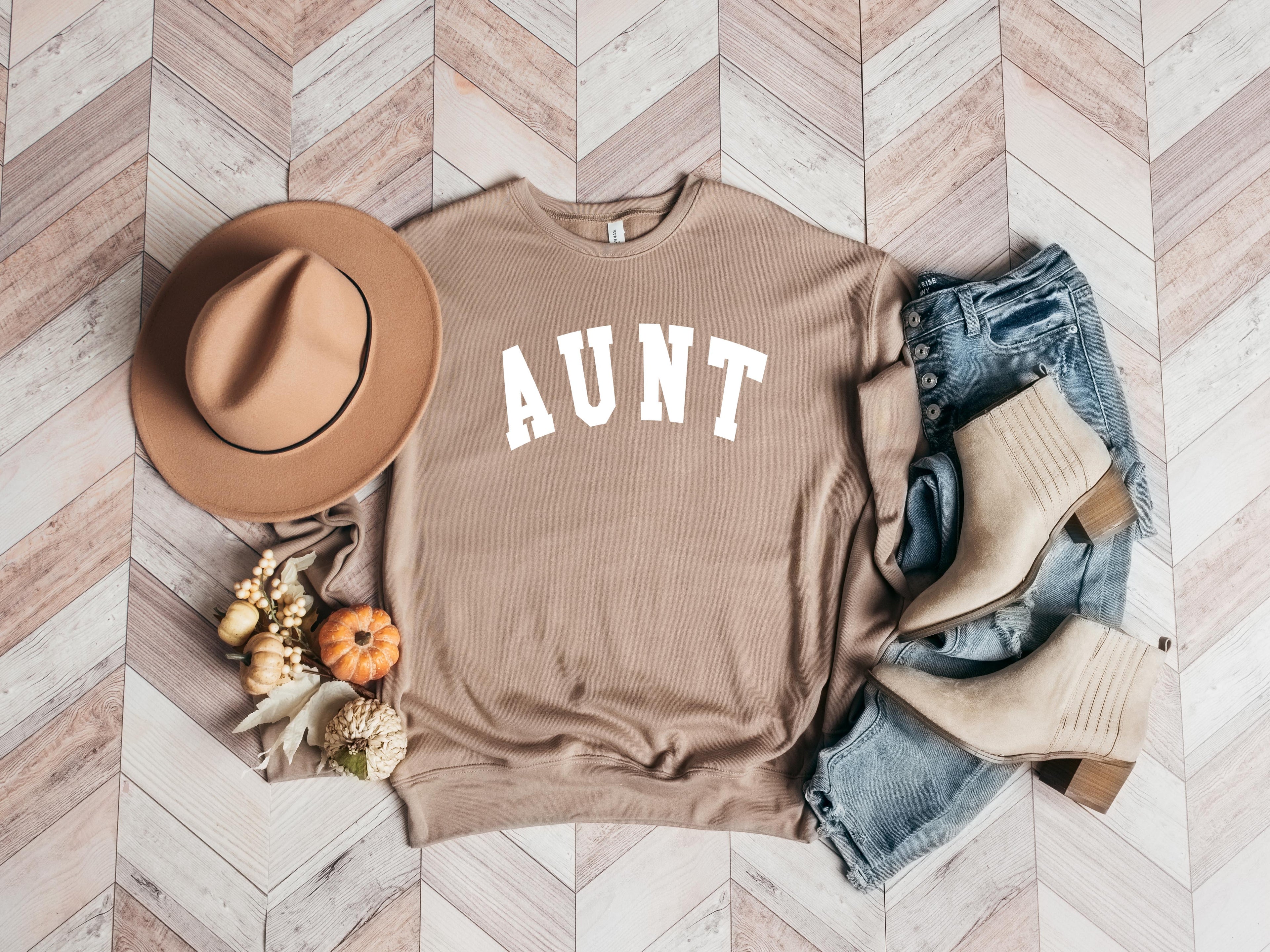 Tan crewneck sweatshirt with bold white "AUNT" graphic on the front