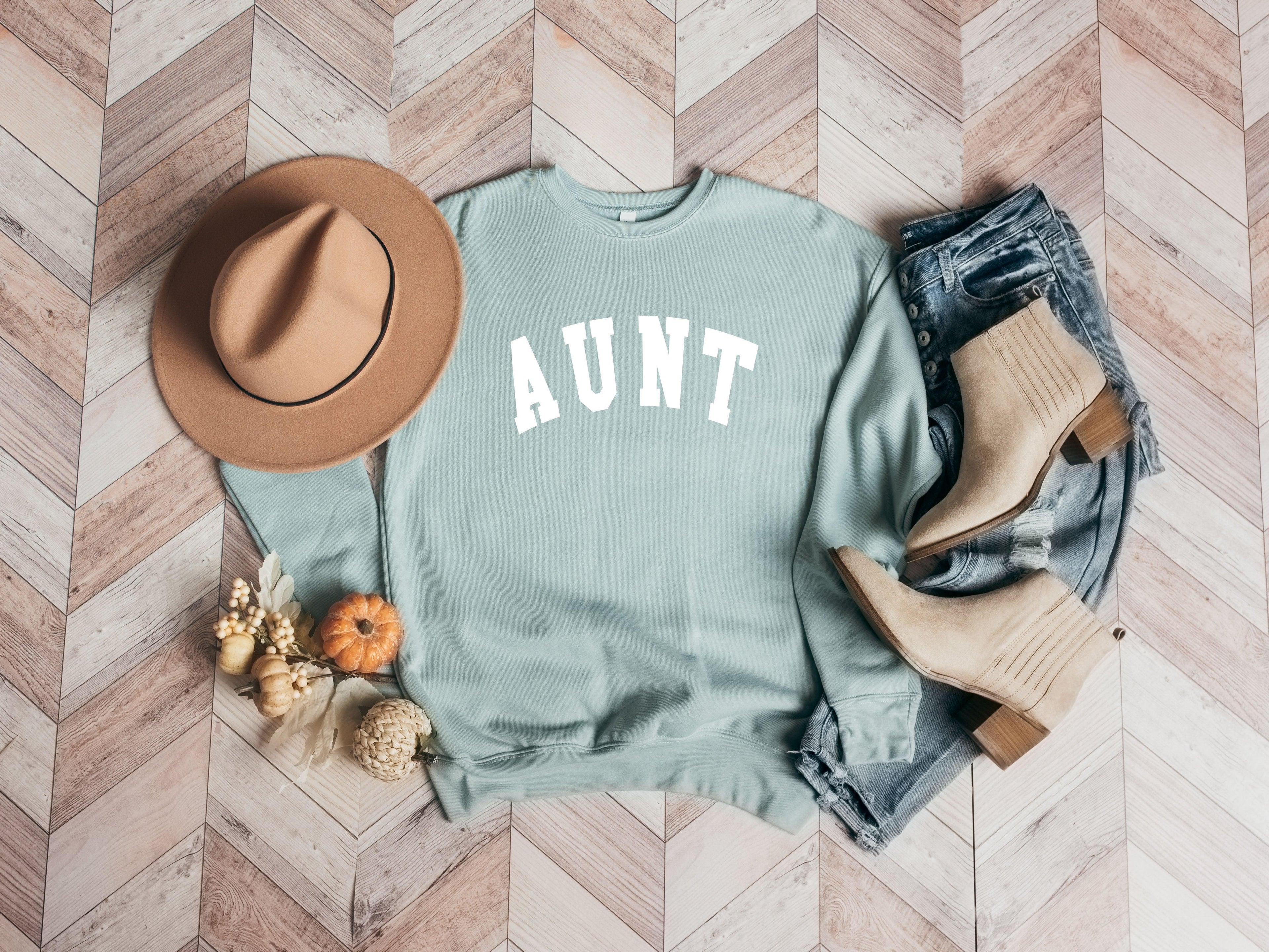 Dusty blue crewneck sweatshirt with large white "AUNT" graphic on the front