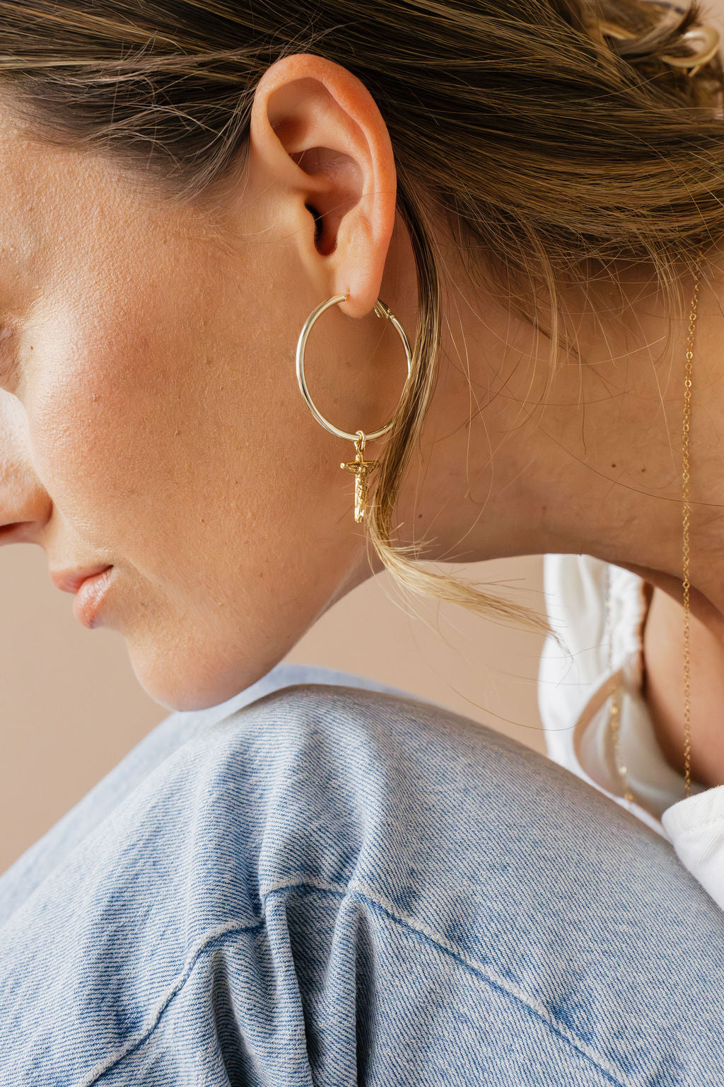 Gold-tone hoop earring with crucifix cross charm on ear, side view