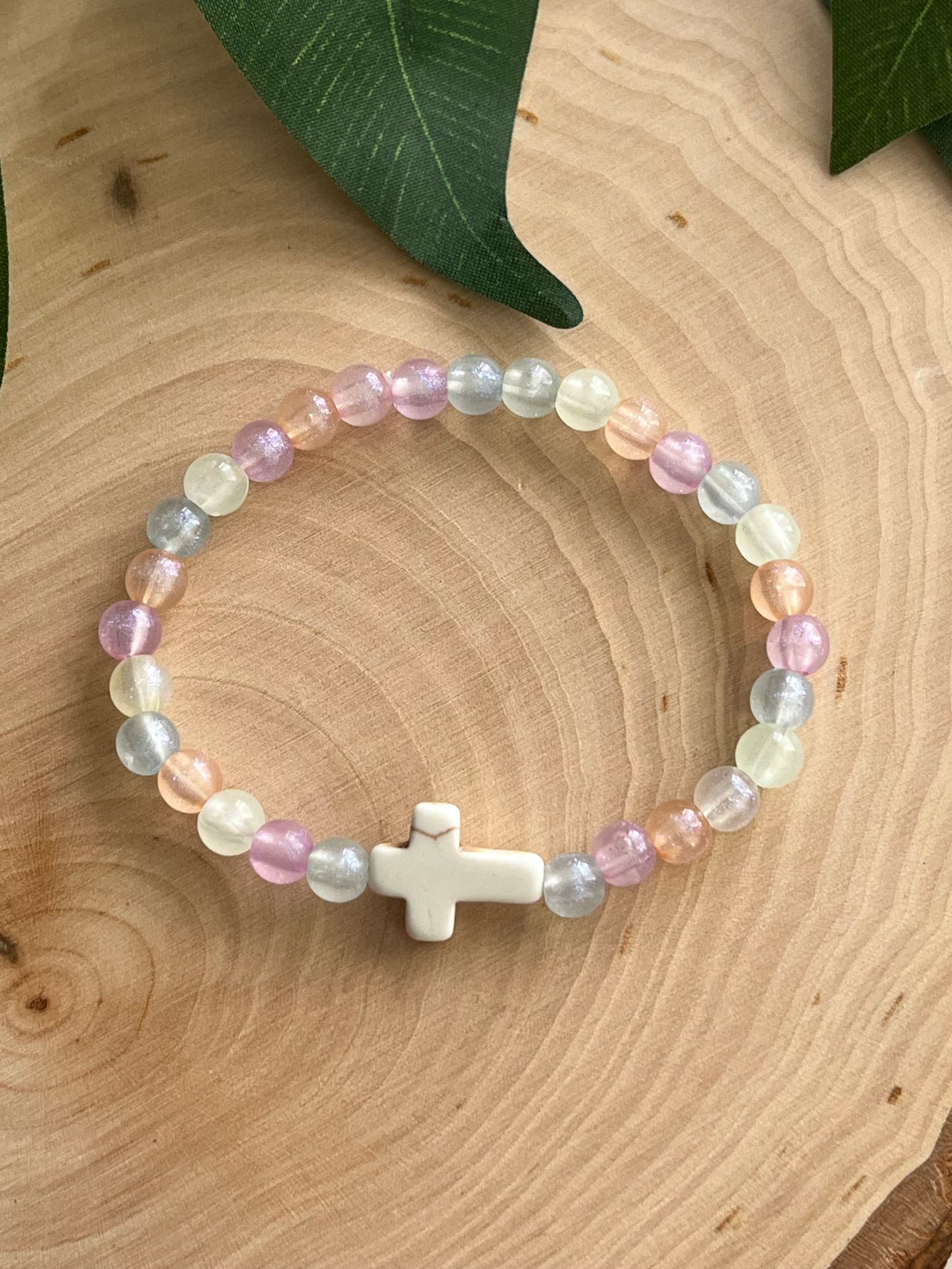 Colorful bead bracelet with a white cross charm and pastel purple, blue, and cream beads.