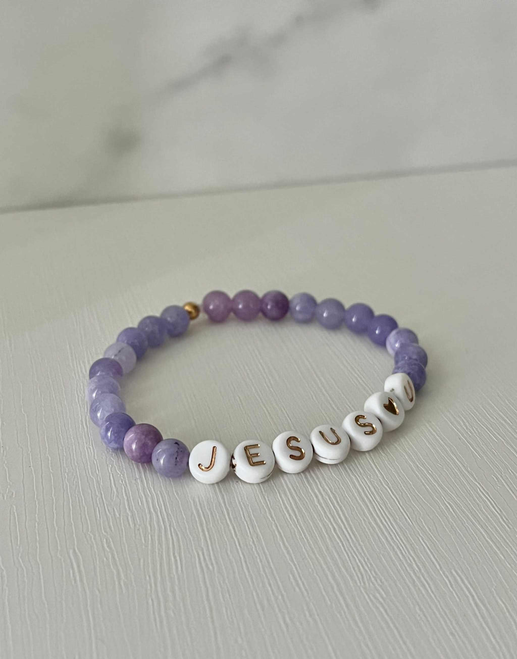 Purple bead bracelet with white letter beads spelling "JESUS U"