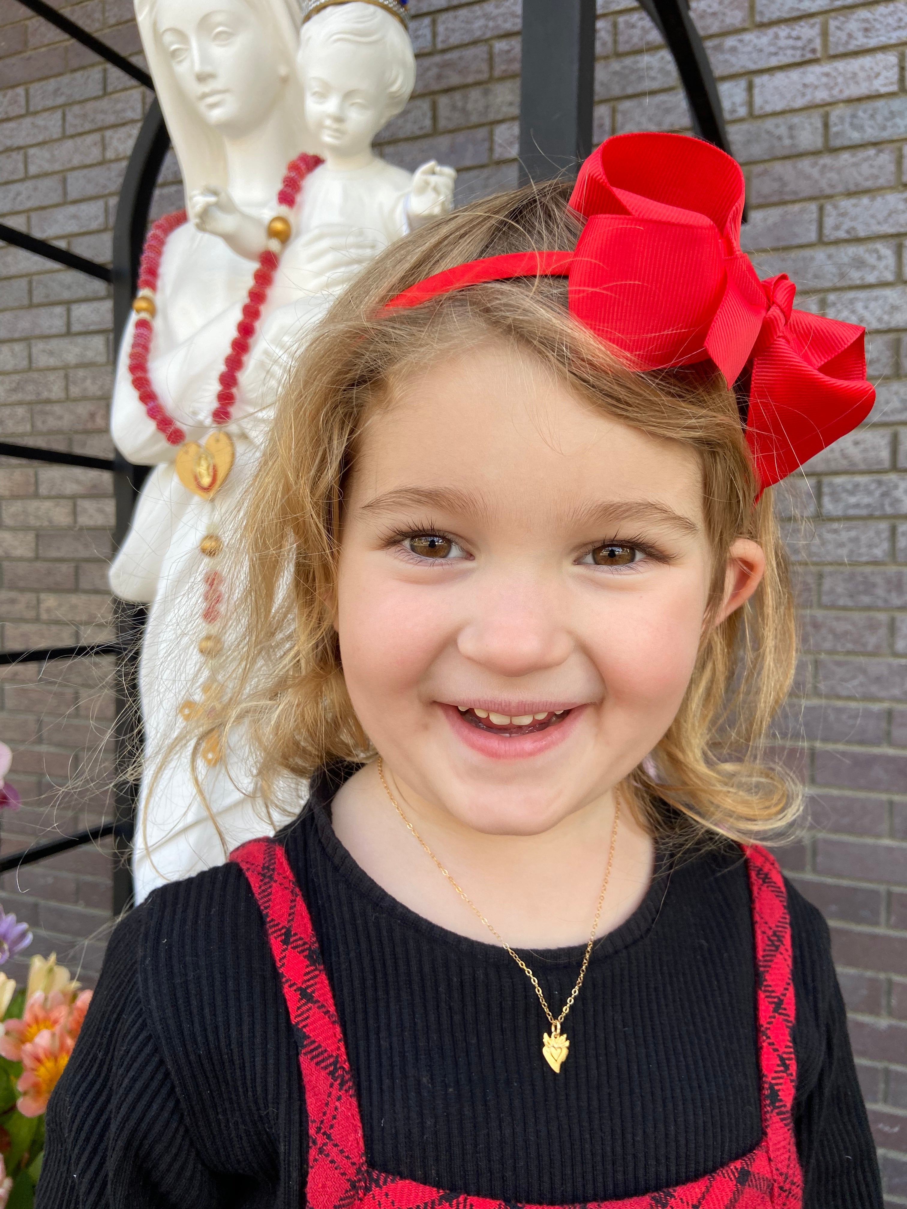 Gold heart pendant necklace with tiny sacred-heart charm on a child