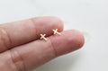 Gold-tone cross stud earrings with two small cross charms on a fingertip.