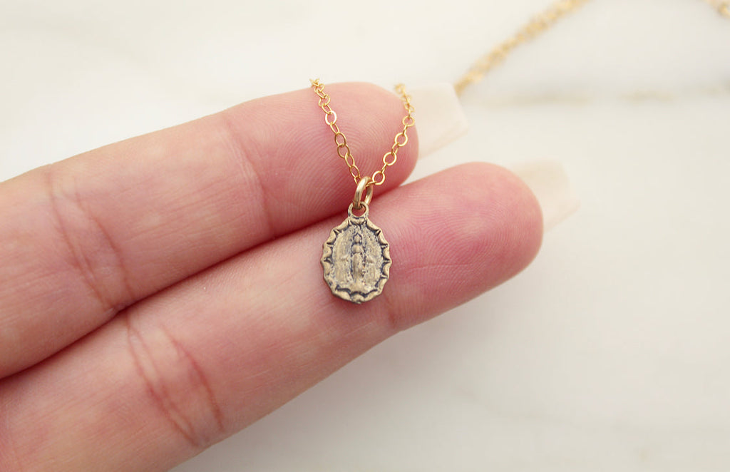 Bronze medal pendant on gold chain, small cameo shape in hand.