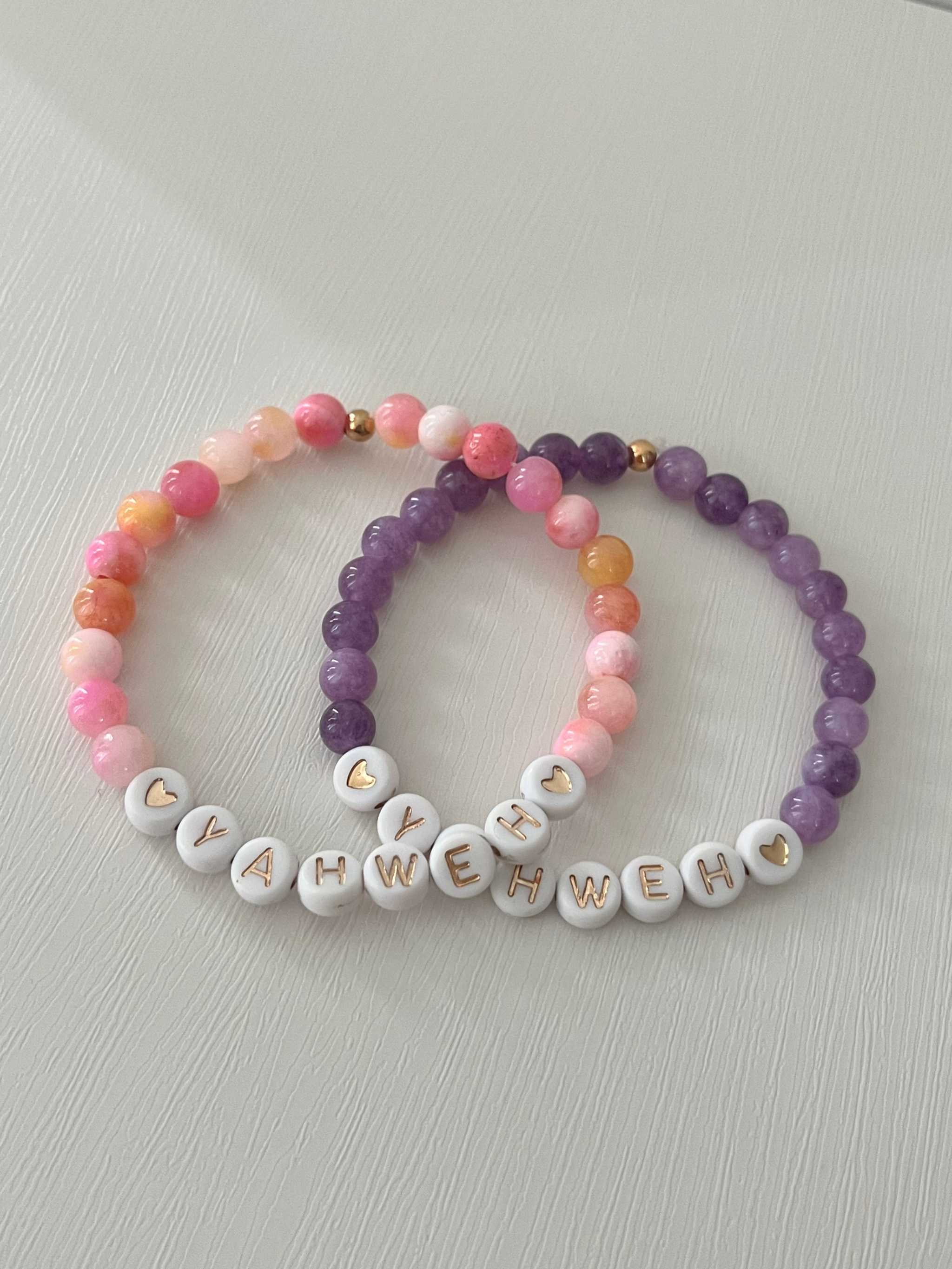 Set of beaded stretch bracelets: pink and purple beads with white letter charms spelling YAHWEH.