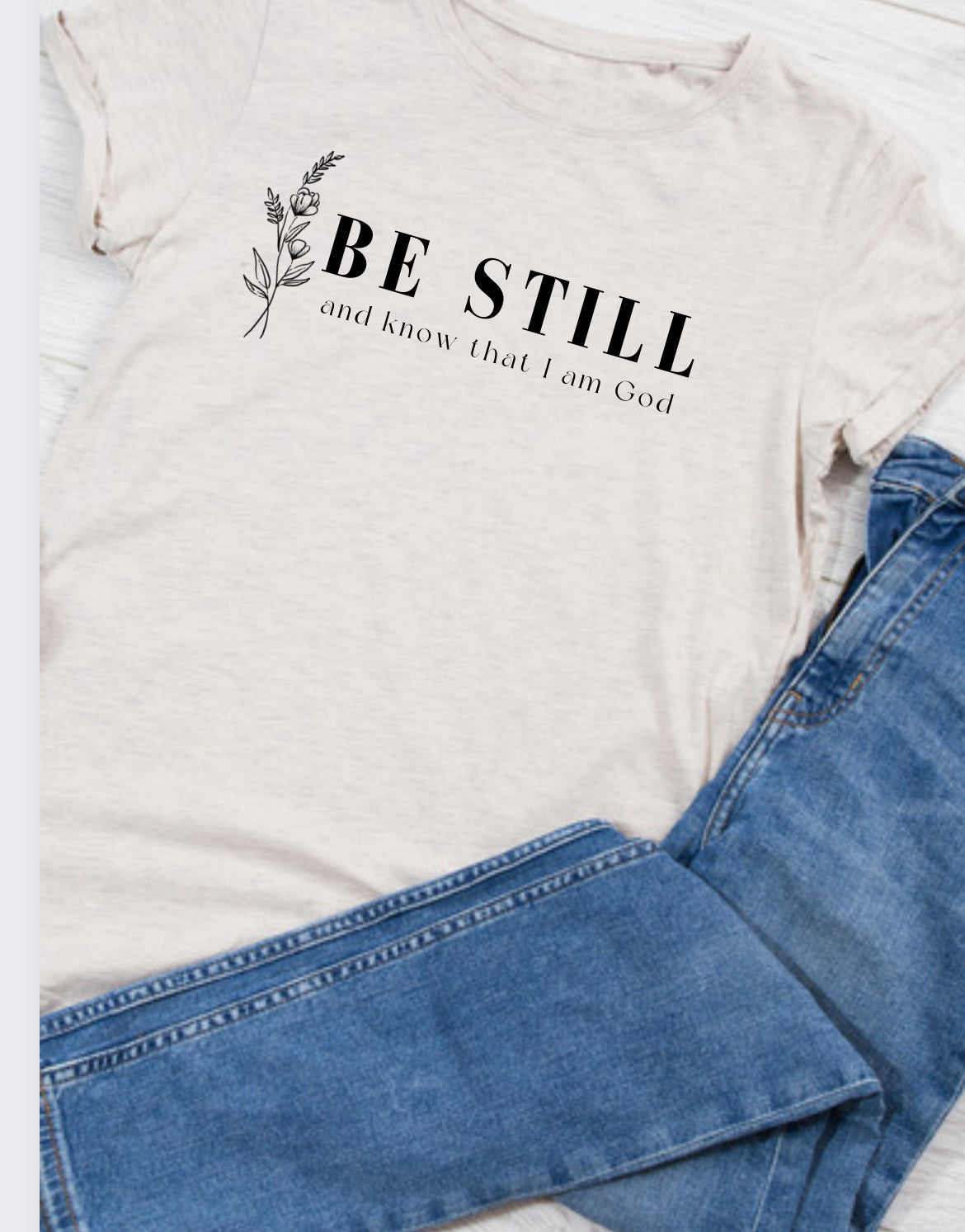 Cream T-shirt with BE STILL scripture text and small floral branch graphic